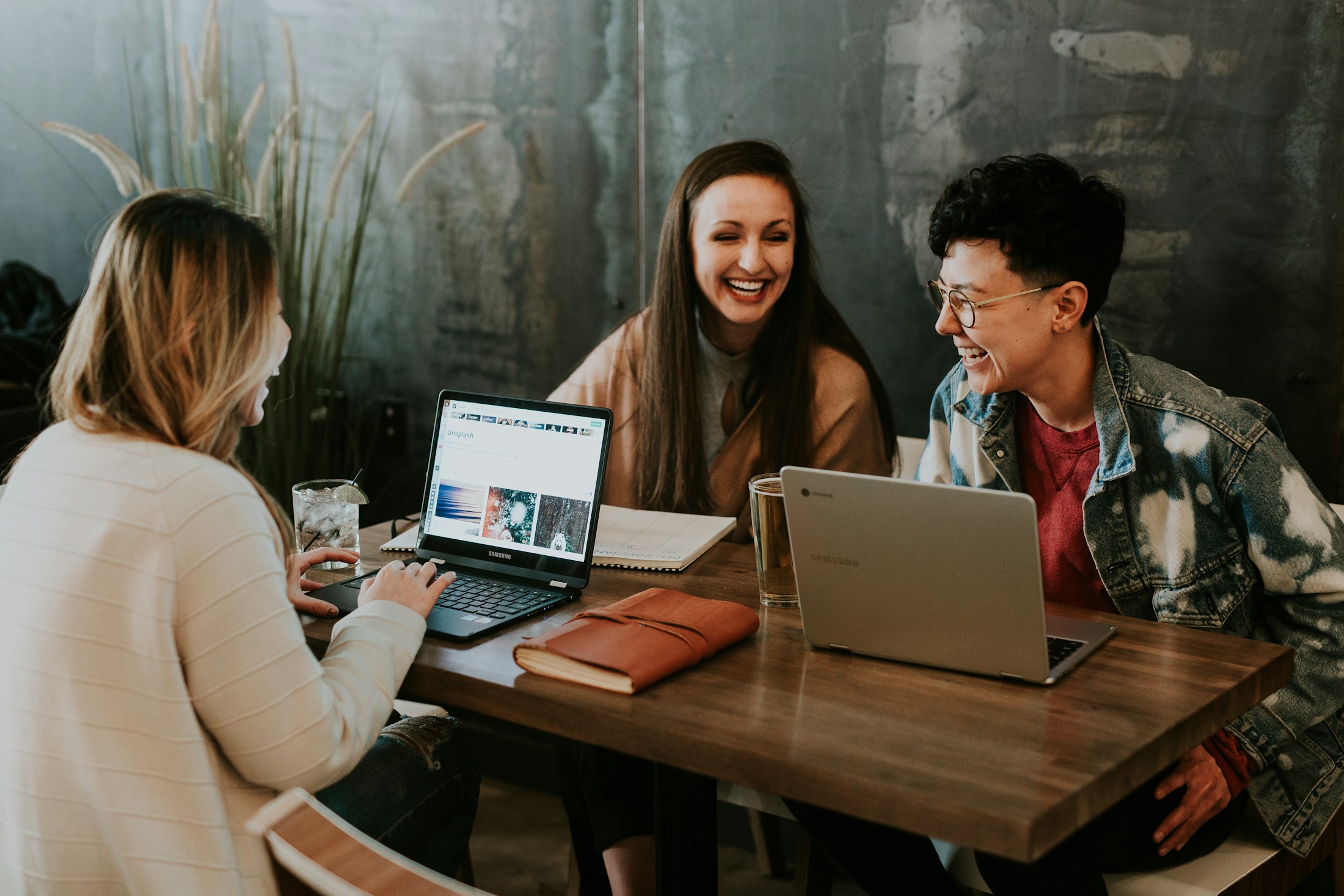 Three colleagues laughing together while working on laptops